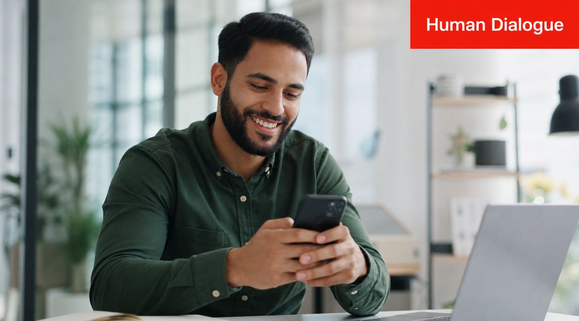 A smiling young man in a green shirt using a smartphone while working in an office.